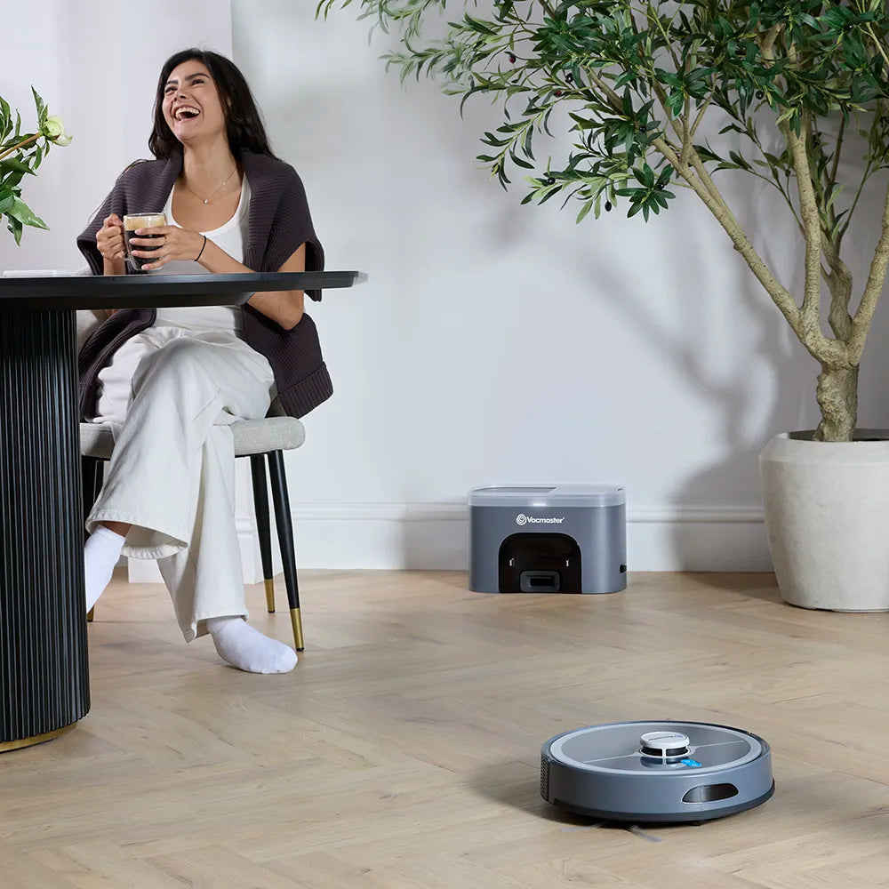 Vacmaster Robot Vacuum Cleaner with dock in modern open plan diner with woman drinking coffee 