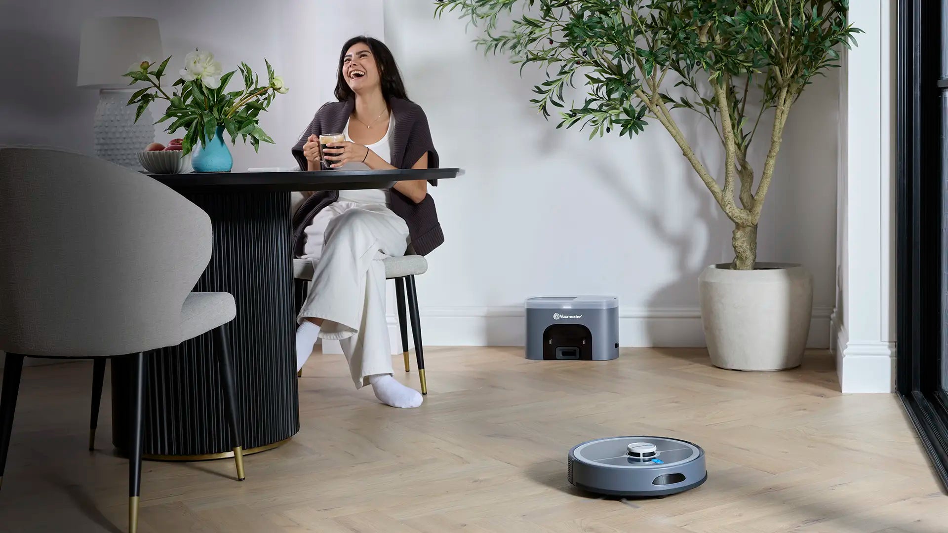 Vacmaster REi Robot Vacuum Cleaner with Self-Empty Station in open plan kitchen with woman relaxing