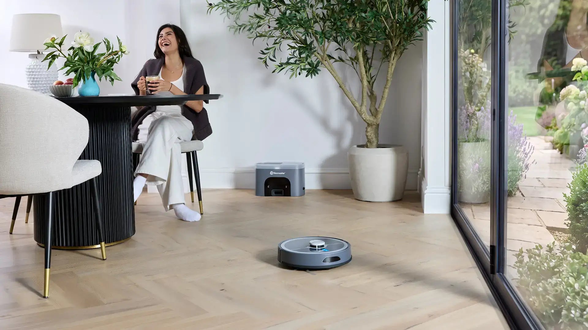 Vacmaster REi Robot Vacuum Cleaner with Self-Empty Station in open plan kitchen with woman relaxing 