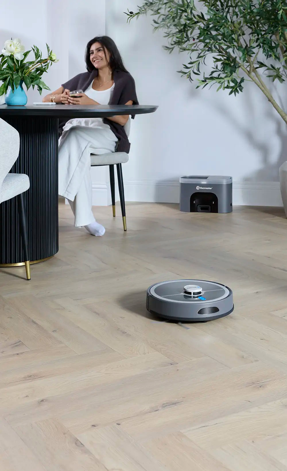 Vacmaster REi Robot Vacuum Cleaner with Self-Empty Station in open plan kitchen with woman relaxing mob